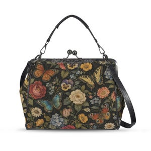May include: A black handbag featuring a floral and butterfly print in shades of orange, yellow, blue, and red. The bag has a dark metal frame with a kiss-lock closure, a top handle, and a detachable shoulder strap with black leather-like trim.