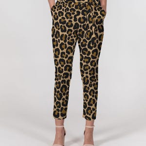Op de afbeelding: Luipaardprint broek in beige en zwart, met een bijpassende stoffen riem. De broek met hoge taille heeft zakken. De stof toont een herhalend patroon van zwarte vlekken op een beige achtergrond.