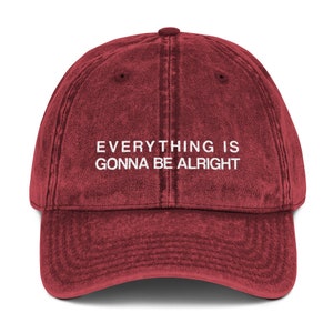 May include: A red vintage baseball cap with the text "EVERYTHING IS GONNA BE ALRIGHT" embroidered in white on the front.