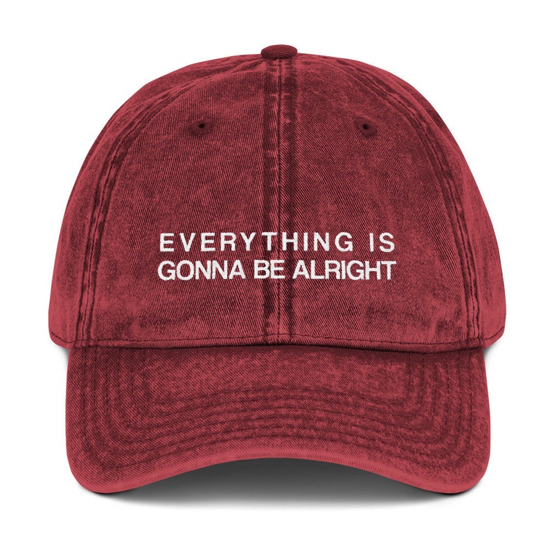 May include: A red vintage baseball cap with the text "EVERYTHING IS GONNA BE ALRIGHT" embroidered in white on the front.