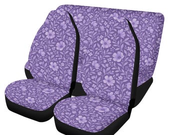 May include: A set of two car seat covers featuring a repeating floral pattern in shades of purple. The design includes various sizes of flowers and leafy vines printed on a light purple background, with solid black side panels and trim.