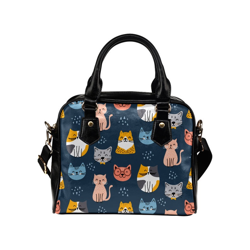 May include: A black leather handbag with a blue and white cat print. The cats are in various poses and have different colored fur. The bag has a top handle and a shoulder strap.