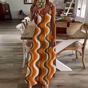 Könnte beinhalten: Ein langes, fließendes Kleid mit einem Retro-Wellenmuster in Braun-, Orange- und Weißtönen. Das Kleid hat einen V-Ausschnitt und Spaghettiträger. Das Kleid hat eine Maxi-Länge.