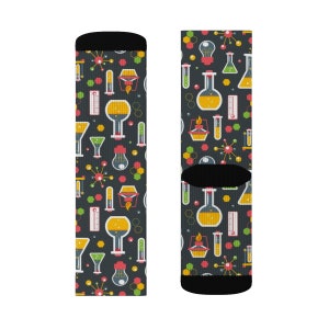 May include: A pair of black socks with a colorful pattern of beakers, test tubes, and other science-related imagery. The socks are designed for adults.