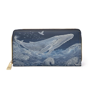 May include: A navy blue wallet featuring a detailed illustration of a whale in the ocean. The design includes white line art of waves, a whale, and birds. The wallet has a gold zip and a rectangular shape.