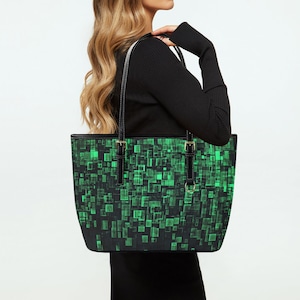 May include: A black tote bag with a green and black geometric pattern. The bag has two black straps and a gold buckle.