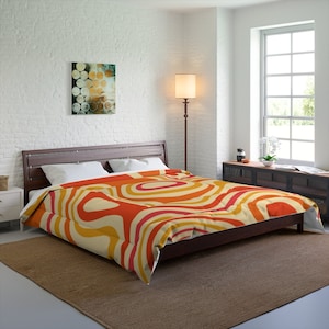 Pode incluir: Uma cama com uma estrutura de madeira marrom e uma capa de edredom com padrão branco e laranja. A capa de edredom apresenta um design geométrico com linhas curvas em tons de laranja, amarelo e branco.