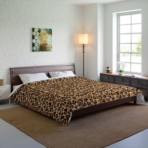 May include: A brown and black leopard print duvet cover on a bed with white pillows. The bed is in a bedroom with a white brick wall, a lamp, and a window.