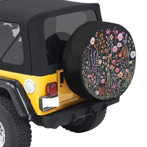 May include: A yellow Jeep with a black spare tire cover featuring a floral design. The tire cover has a black background with colorful flowers and greenery.