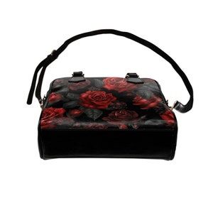 May include: A black satchel handbag with a red rose floral print. The bag has a top handle and a long adjustable shoulder strap.