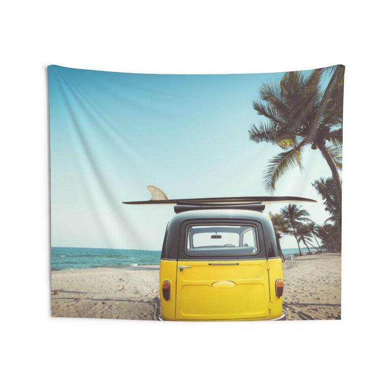 May include: A yellow vintage van with a black roof and a surfboard strapped to the top. The van is parked on a sandy beach with palm trees in the background.