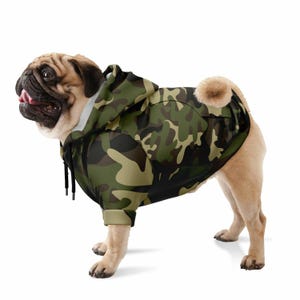 May include: A pug dog wearing a green, black, and brown camouflage hooded sweatshirt. The sweatshirt has a drawstring hood and long sleeves.