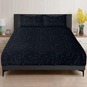 May include: A dark navy blue bed set with a constellation design featuring teal and gold stars. The set includes a duvet cover and two pillowcases. The bedding is on a grey bed frame on a wooden floor.