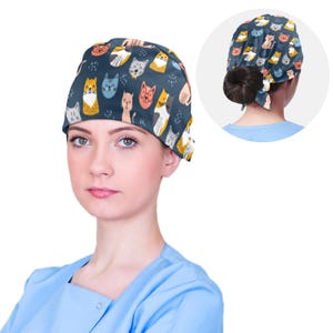 Può includere: Un berretto chirurgico blu con una stampa di gatti colorati. Il berretto ha un laccio sul retro ed è indossato da una persona con una camice chirurgica blu.