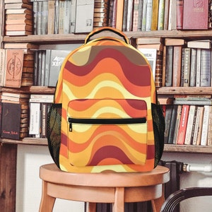May include: A yellow, orange, and red backpack with a wavy pattern. The backpack has a black zipper and a mesh pocket on each side.