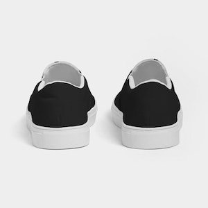 May include: A pair of black canvas slip-on shoes with white soles. The shoes are shown from the back.