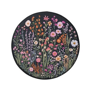 May include: A circular embroidery hoop with a black background and a colorful floral design. The design features pink, orange, and white flowers with green stems and leaves.