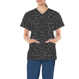 Puede incluir: Una blusa de trabajo gris con estampado de leopardo negro. La blusa tiene cuello en V y dos bolsillos.