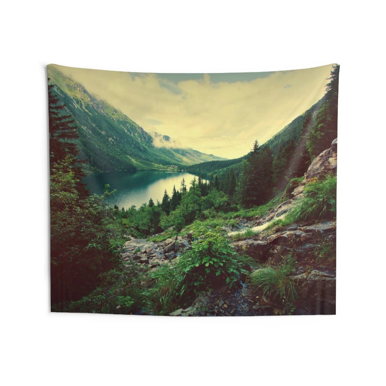 May include: A scenic tapestry featuring a mountain lake surrounded by lush green trees and a rocky hillside. The lake is calm and reflects the cloudy sky above. The image has a vintage, faded look.