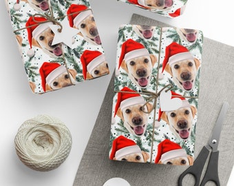 Op de afbeelding: Kerstcadeaupapier met een herhaald patroon van een gele Labrador Retriever met een kerstmuts. De achtergrond bevat groene dennentakken en witte accenten. Er zijn verschillende ingepakte cadeaus te zien.