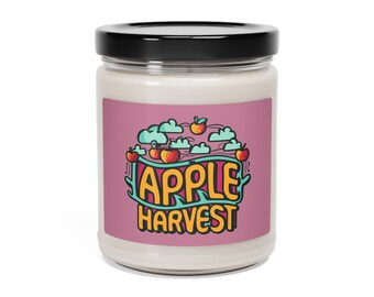 Puede incluir: Una vela blanca en un tarro de cristal con tapa negra. La etiqueta presenta las palabras "APPLE HARVEST" en un diseño colorido con manzanas y nubes. El fondo de la etiqueta es rosa.