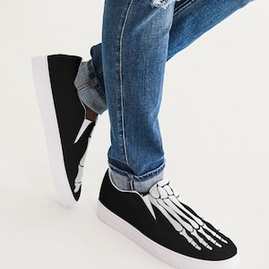 May include: Black slip-on canvas shoes with a white skeleton foot design. The shoes have a white rubber sole.