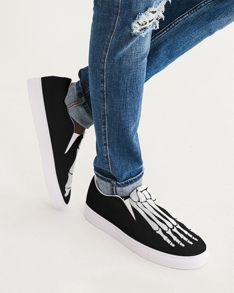 May include: Black slip-on canvas shoes with a white skeleton foot design. The shoes have a white rubber sole.