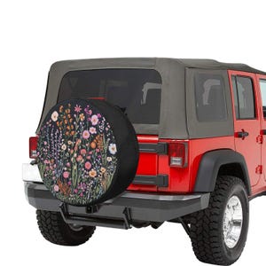 May include: A red Jeep Wrangler with a black spare tire cover featuring a floral pattern. The spare tire cover has a black background with colorful flowers and leaves.
