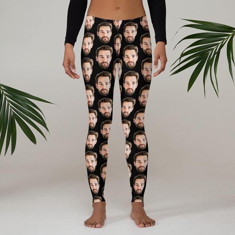 May include: Black leggings featuring a repeating pattern of a man's face. The faces are evenly spaced across the fabric. The leggings are worn by a person with a black long-sleeve shirt.