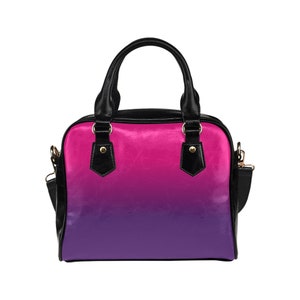 May include: A black handbag with a pink to purple ombre design. The bag has a top handle and a shoulder strap.