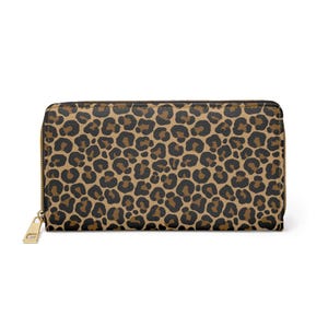 Puede incluir: Una cartera rectangular con cremallera y tirador dorados. La cartera presenta un estampado de leopardo marrón y negro. La cremallera está en la parte superior y se extiende por tres lados de la cartera. La cartera está cerrada.