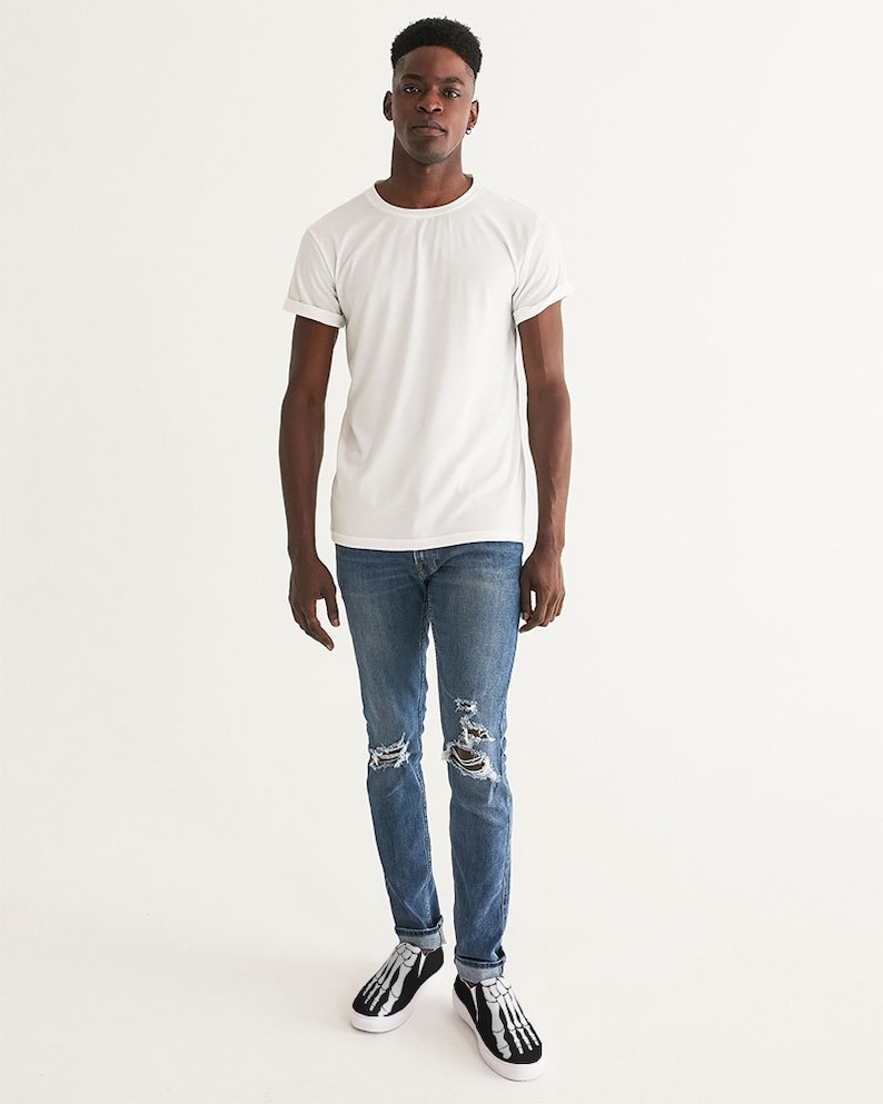 May include: A person wearing a white t-shirt, blue jeans with distressed details, and black and white skeleton-themed sneakers.