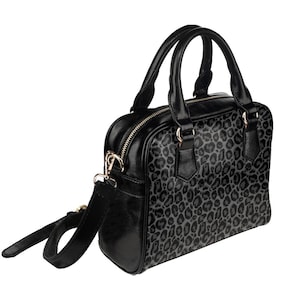 May include: A black satchel handbag with a leopard print design. The bag has a top handle and a detachable shoulder strap.