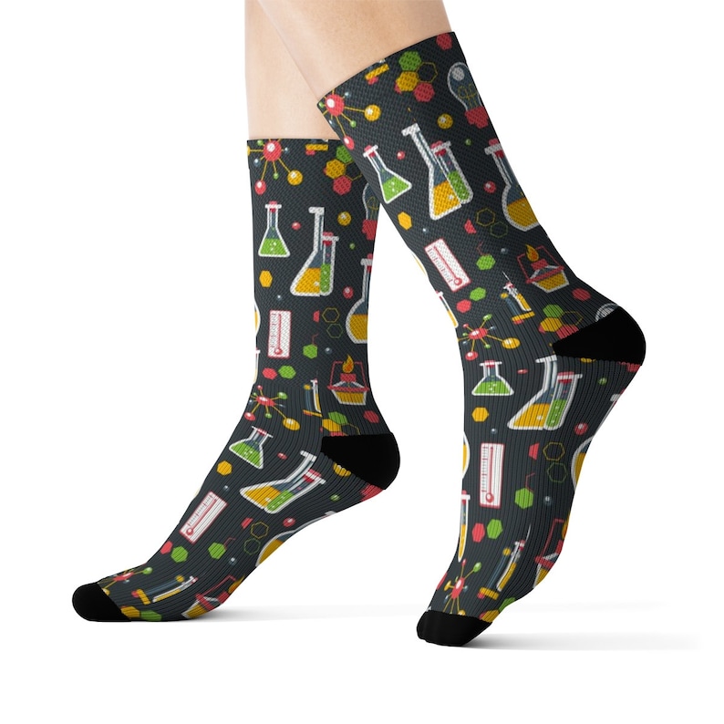 May include: A pair of black socks with a colorful science themed pattern. The pattern features beakers, molecules, and thermometers.