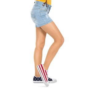 Puede incluir: Pantalones cortos vaqueros azul claro con dobladillos. La persona lleva zapatillas de lona blancas con un dise&ntilde;o de rayas rojas y blancas en el lateral y un estampado de estrellas azul marino en el tal&oacute;n.