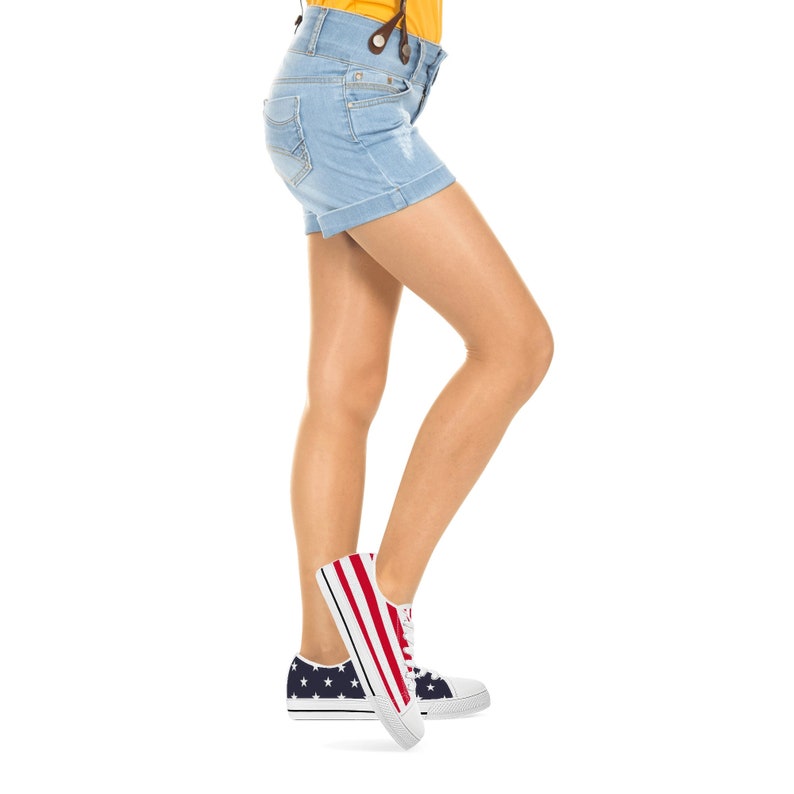 Puede incluir: Pantalones cortos vaqueros azul claro con dobladillos. La persona lleva zapatillas de lona blancas con un dise&ntilde;o de rayas rojas y blancas en el lateral y un estampado de estrellas azul marino en el tal&oacute;n.