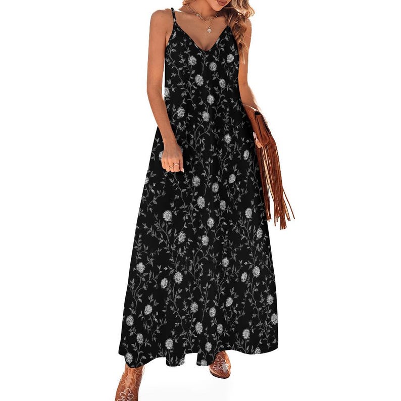 May include: A black maxi dress with a floral pattern. The dress features a V-neckline, spaghetti straps, and a flowing skirt. The floral design is in white and gray, creating a contrasting effect against the black fabric. The dress is suitable for casual or semi-formal occasions.