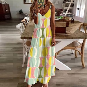 Peut inclure: Une longue robe sans manches avec un décolleté en V. La robe présente un motif répétitif d'ovales colorés qui se chevauchent en jaune, rose, vert et blanc. La robe est faite d'un tissu léger et a une silhouette fluide.