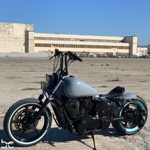 May include: A custom-built motorcycle with a gray gas tank, black engine, and black wheels with whitewall tires. The motorcycle has a solo seat and a sissy bar.
