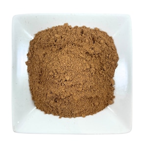 May include: A small white square dish filled with a mound of light brown ground cinnamon powder.