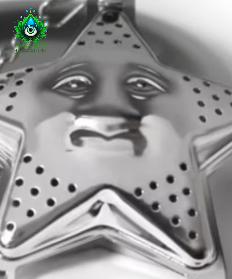 May include: A silver-toned metal tea infuser shaped like a five-pointed star. The surface features a molded face with eyes, a nose, and a mouth, along with small circular perforations across the star points for steeping loose leaf tea.