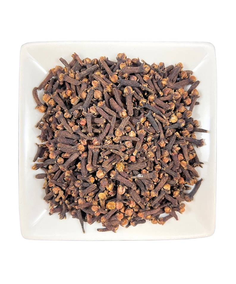 May include: A white square dish filled with a large pile of dried brown cloves.