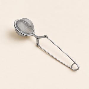 Puede incluir: Un infusor de té de acero inoxidable de color plateado con una cesta de malla esférica unida a un mango de estilo tijera con resorte. El mango incluye un pequeño lazo circular en el extremo para colgarlo, y la malla permite infusionar té.