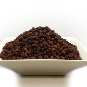 May include: A white square dish filled with a mound of dried, dark brown and reddish-brown peppercorns.