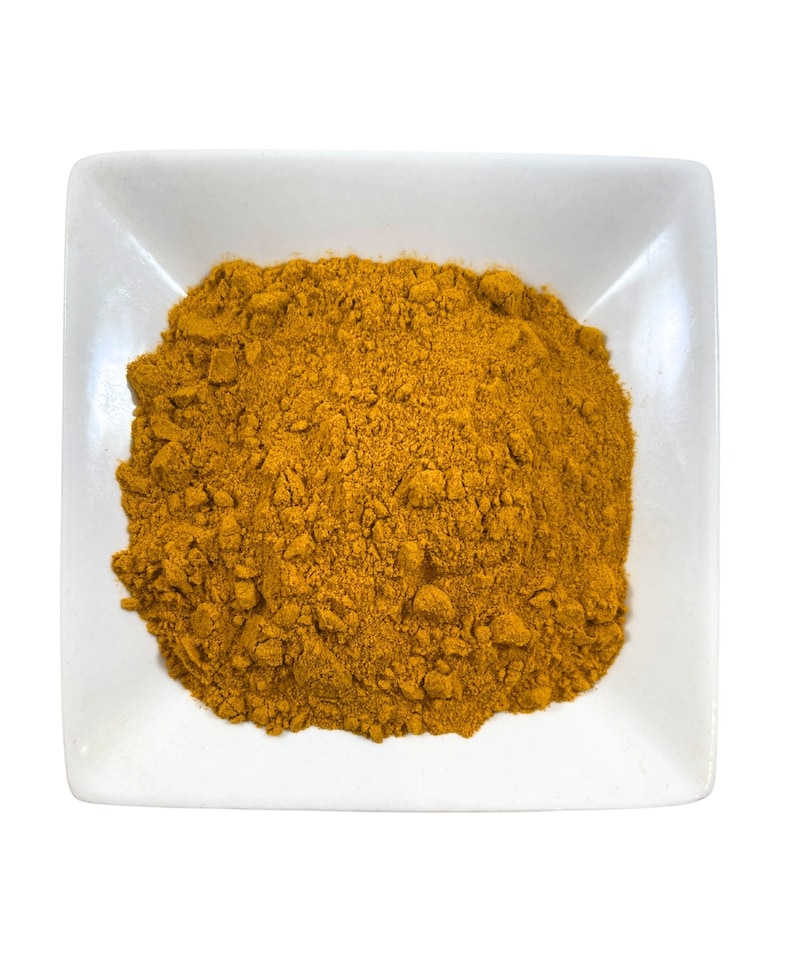 May include: A small white square dish filled with a mound of bright yellow turmeric powder.