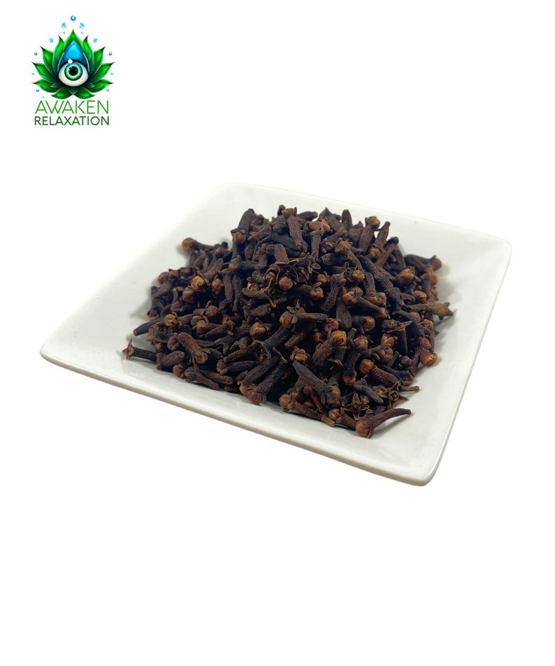 May include: A white square plate filled with dried whole cloves. The cloves are dark brown and have a slightly reddish hue.