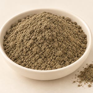 Puede incluir: Un peque&ntilde;o cuenco redondo de cer&aacute;mica de color blanco roto lleno de un mont&oacute;n de polvo fino, terroso y de color gris oliva. La textura del polvo parece seca y granulada, con un peque&ntilde;o mont&oacute;n de la misma sustancia gris esparcido a la derecha.