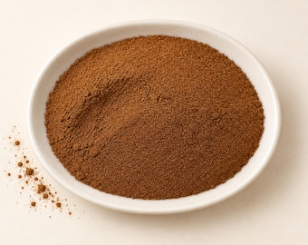 Pode incluir: Uma tigela de cerâmica branca cheia com um monte de canela em pó finamente moída, de cor castanho-média. A textura da especiaria é uniforme e em pó, com uma pequena quantidade de pó de canela espalhada fora da borda da tigela.