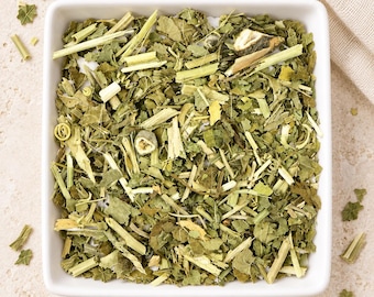 May include: A square white ceramic bowl filled with a mixture of dried green leaves, light green fibrous stems, and small curled tendrils. The mixture contains various shades of green, ranging from pale yellow-green to deep forest green.
