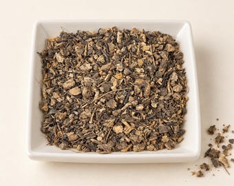 May include: A square white ceramic bowl filled with a mixture of dried, chopped dark brown and tan root pieces. The texture is coarse and irregular, consisting of small, fragmented botanical bits scattered throughout the container.